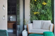 a modern and bright balcony with a living wall, a cozy loveseat, bright wicker side tables and a teal woven chair plus some blooms