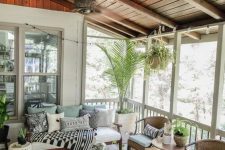 a modern boho screened porch with simple stained wood and rattan furniture, a glass coffee table, potted plants and printed textiles