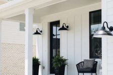 a modern farmhouse porch with layered rugs, a black chair and black planters, greenery, printed textiles and sconces