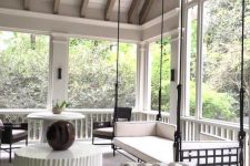 a modern screened porch with a hanging bench, black wicker chairs, side and coffee tables, some plants and cool views