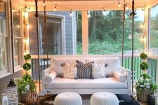 a modern screened porch with a white hanging sofa, potted plants and blooms, candle lanterns and white poufs plus a graphic rug
