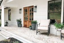 a neutral and simple farmhouse porch clad with bricks, with neutral furniture, potted greenery and plants is a welcoming and cool space