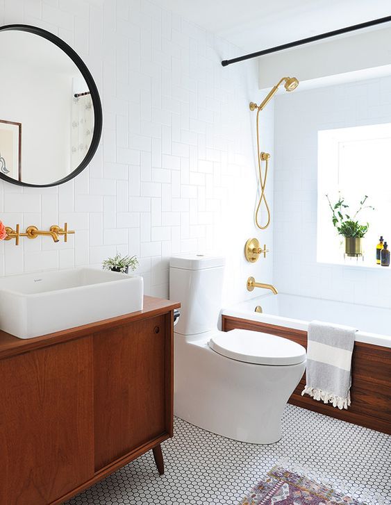 A neutral mid century modern bathroom with geometric and penny tiles, a tub clad with wood and a stained vanity, gold fixtures
