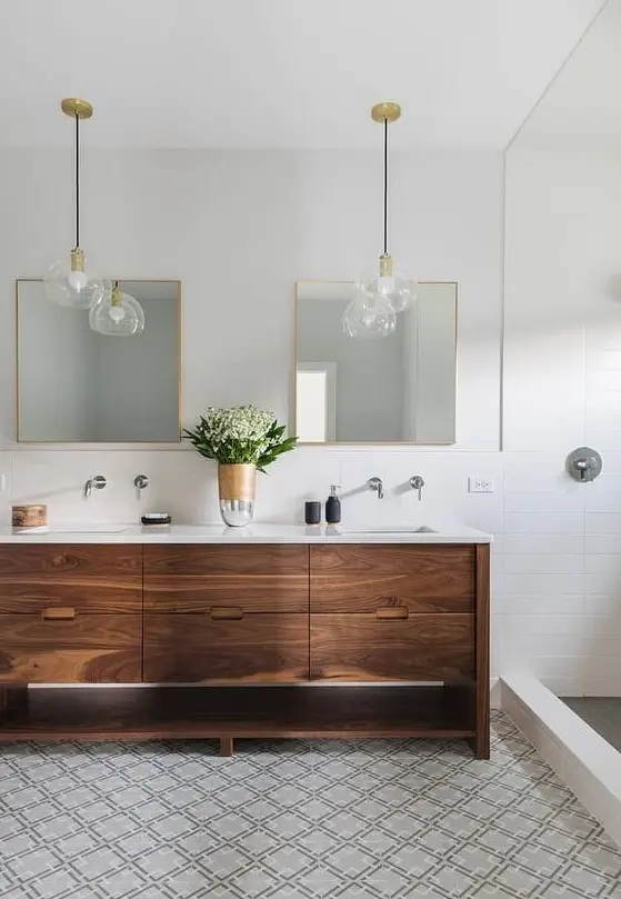 A neutral mid century modern bathroom with white and mosaic geo tiles, a wooden vanity and chic pendant lamps plus mirrors in gold frames