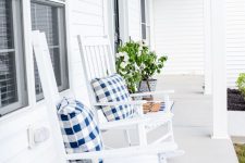 a pretty and airy summer farmhouse porch done in white, with white rockers, potted greenery and lanterns on the wall