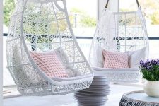a pretty small patio with cool white hanging chairs with printed pillows, side tables, potted blooms is a very chic space to relax in