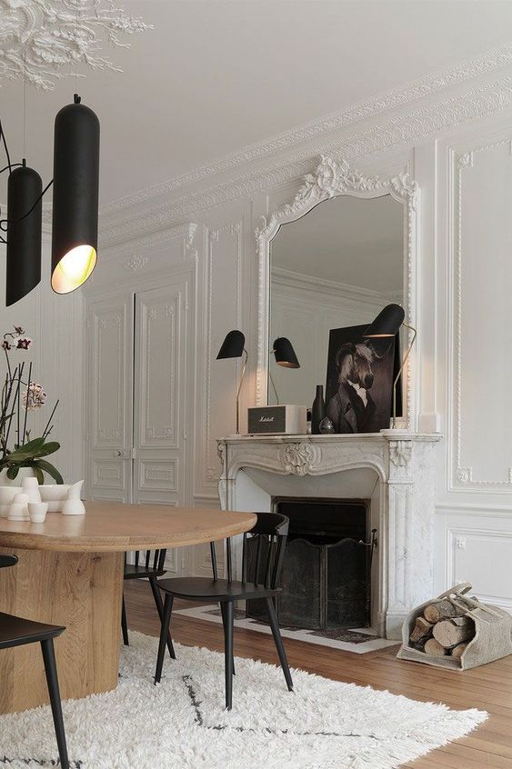 a refined Parisian home office with molding on the walls, ceiling and fireplace, a rounded desk, black chairs, black lamps and art