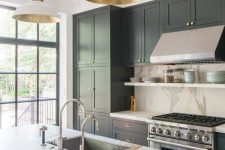 a refined kitchen with dark grey cabinets, a white stone backsplash and countertops, pendan lamps with gold parts and chromatic appliances and fixtures