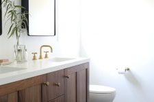 a refined mid-century modern bathroom with black hex tiles, a stained vanity, a printed boho rug, gold fixtures and sconces
