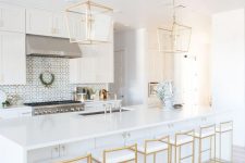 a refined white kitchen with chrome appliances and fixtures and beautiful gold pendant lamps and gold and white stools