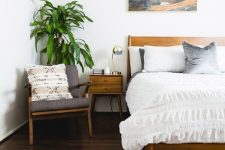 a relaxed mid-century modern bedroom with a dark stained floor, stained furniture, a pretty photo over the bed, pendant lamps and a potted tree