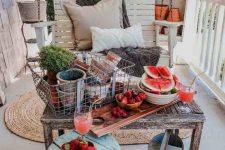a relaxed rustic porch with a hanging bench, a shabby table with a metal crate and planters, a watering can and a shabby stool