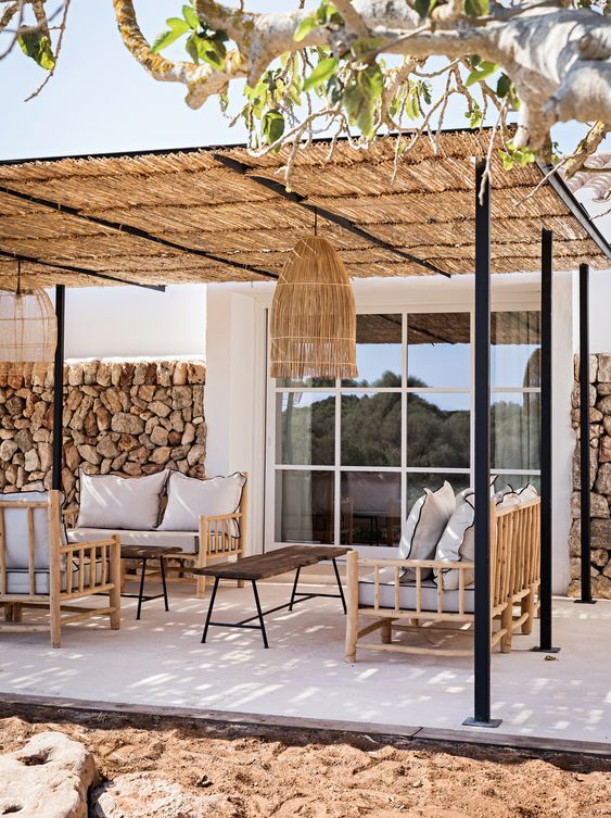 a relaxed tropical patio with a roof, a rock wlal, bamboo and wood furniture, a woven pendant lamp and neutral textiles and upholstery
