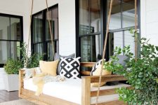 a rustic porch with a hanging bench, potted greenery, a rug and printed textiles is a lovely and inspiring space to be