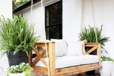 a simple and cute porch space with a hanging daybed of wood, with potted plants and a printed rug is very welcoming