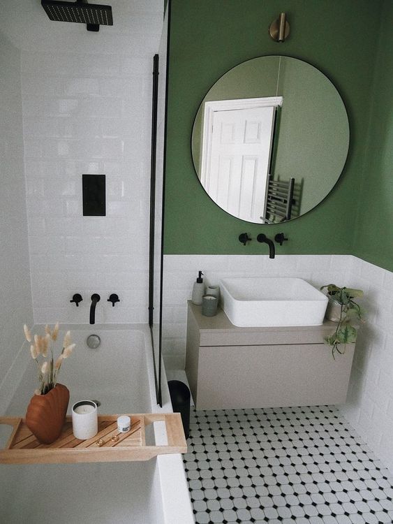 a small and cool mid-century modern bathroom with green walls, white subway tiles, a tub with a shower, a floating vanity and a round mirror