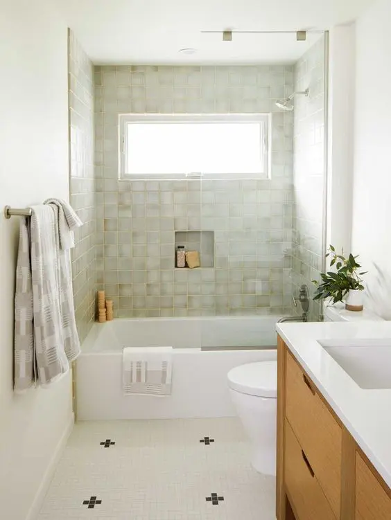 A small and elegant mid century modern bathroom with green and black and white tiles, a tub, a stained vanity and some neutral towels