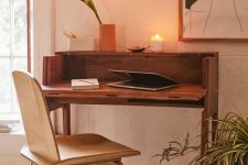 a small and lovely mid-century modern working space with a small stained desk and a plywood chair, a cool artwork and a floor lamp