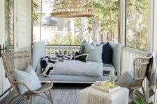 a small and welcoming coastal screened porch with rattan chairs, a soft blue sofa, a pouf, a woven pendant lamp and a potted plant