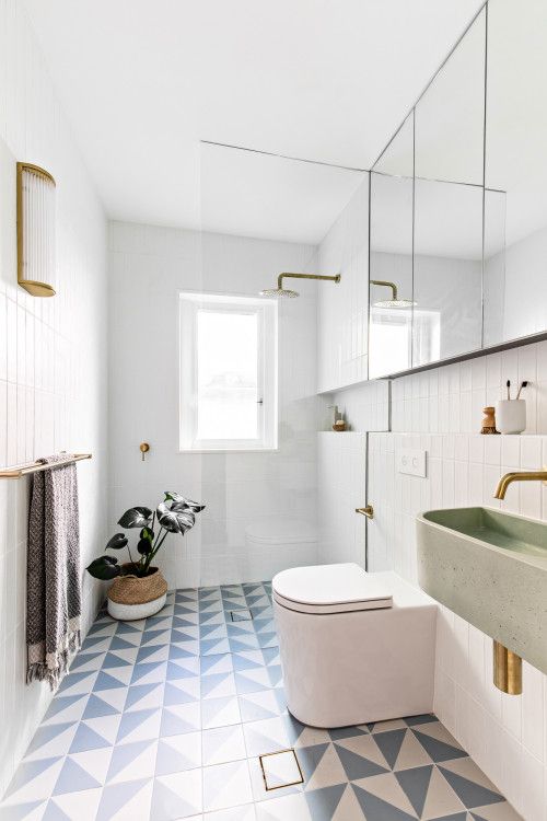 A small mid century modern bathroom with white skinny and geo blue and white tiles, a shower space, a mirror cabinet, a green sink and gold fixtures
