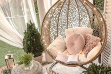 a small outdoor nook with mosquito nets, a hanging rattan chair, lights, candle lanterns and greenery around is a dreamy space to be