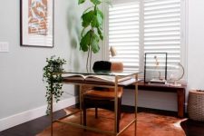 a small working space with a tiered desk, a leather chair, a faux animal skin rug, a console table with some artworks and potted plants