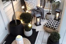a small yet inviting balcony in black and white, with a rattan chair, candle lanterns, potted plants and some lights is a gorgeous idea