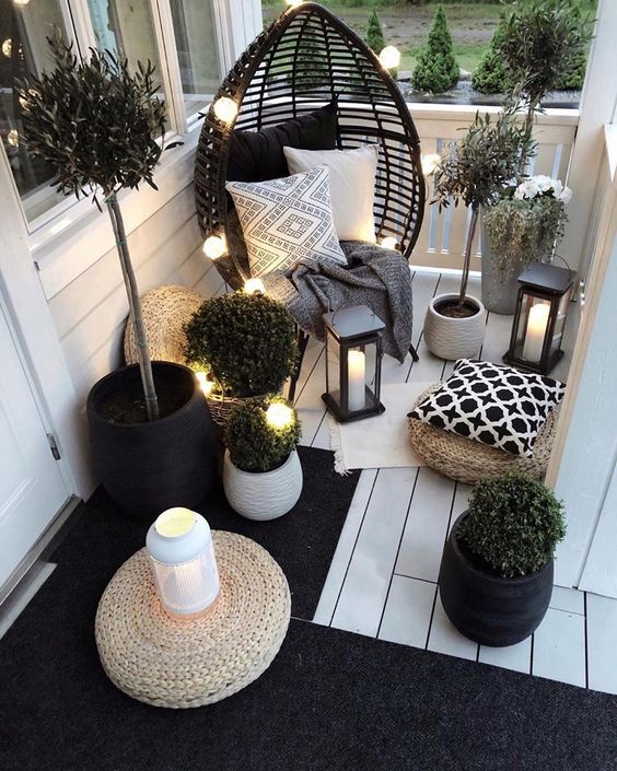 a small yet inviting balcony in black and white, with a rattan chair, candle lanterns, potted plants and some lights is a gorgeous idea