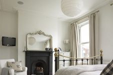 a sophisticated Victorian bedroom in neutral shades, with a metal built-in fireplace, a metal bed, neutral textiles and a grey dresser plus a mirror