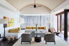a sophisticated mid-century modern living room with two white sofas, a stone coffee table, grey rattan chairs, a colorful artwork and bright mustard pillows