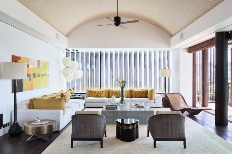 a sophisticated mid century modern living room with two white sofas, a stone coffee table, grey rattan chairs, a colorful artwork and bright mustard pillows