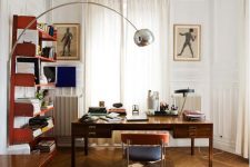 a sophisticated mid-century modern work space with a stained desk, a navy and red chair, red shelves, cool artworks and a floor lamp