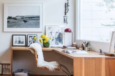 a stylish and light-filled mid-century working space witha  corner desk, some skylights, a rattan chair, cool artworks and a red lamp