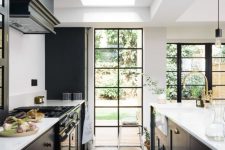 a stylish black kitchen with a large skylight and French windows with black frames, a black hood and a parquet floor is wow