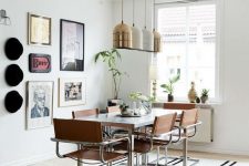 a stylish dining zone with a pretty gallery wall with hats, a marble dining table, leather chairs with chrome legs and pendant gold and white lamps
