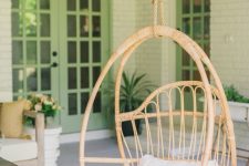 a stylish hanging rattan chair with pillows is a cool idea to style a rustic porch or another outdoor rustic space