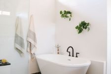 a stylish mid-century modern bathroom with white and black mosaic tiles, a tub, greenery and a black pebble rug