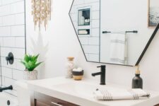 a stylish mid-century modern bathroom with white and black tiles, a hexagon mirror, a wooden vanity and touches of brass