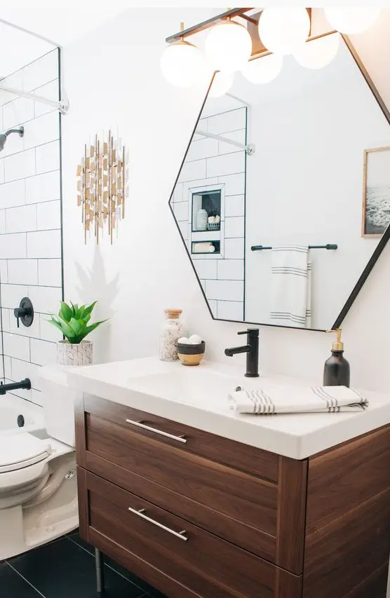 a stylish mid-century modern bathroom with white and black tiles, a hexagon mirror, a wooden vanity and touches of brass