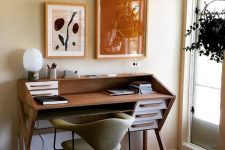 a stylish mid-century modern home office nook with a tiered desk, a green chair, a colorful gallery wall looks bold