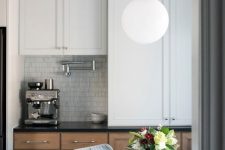 a stylish modern farmhouse kitchen with stained and white cabinets, a bubble lamp on a gold chain, chromatic applainces and handles on the cabients