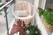 a tiny balcony with wood tiles, a lovely round hanging chair with pillows, a small folding table and potted greenery