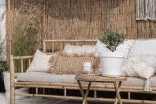 a tropical deck with a roof, a bamboo sofa, a folding side table of bamboo, a jute rug and potted greenery plus macrame hanging