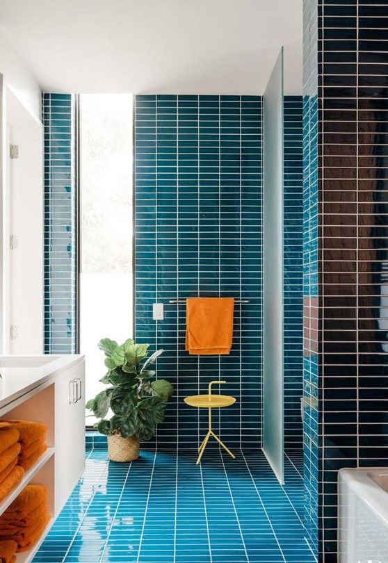 A vibrant mid century modern bathroom clad with navy skinny tiles, a white flaoting vanity and touches of orange
