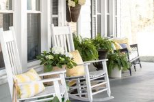 a vintage rustic porch with white rockers and a black vintage bench, potted plants and blooms plus printed pillows is a chic idea