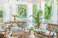 a vintage tropical screened porch with a dining set with folding furniture, wooden chairs and a bench, woven side tables and potted plants