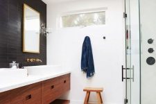 a welcoming mid-century modern bathroom with black and white tiles, a shower space, a double stained vanity, metallic fixtures