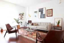 a welcoming mid-century modern living room with a grey sofa, burgundy leather chairs, a chic gallery wall, open shelves, printed pillows and a rug