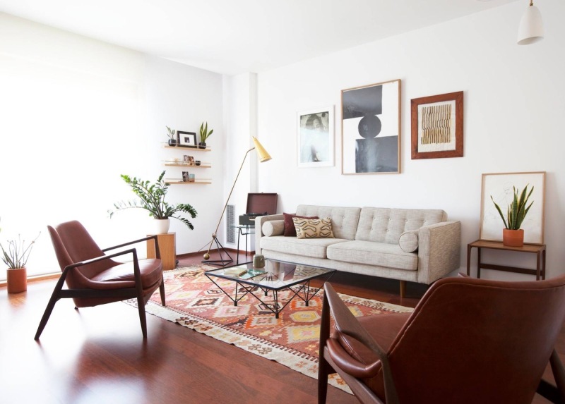 a welcoming mid century modern living room with a grey sofa, burgundy leather chairs, a chic gallery wall, open shelves, printed pillows and a rug