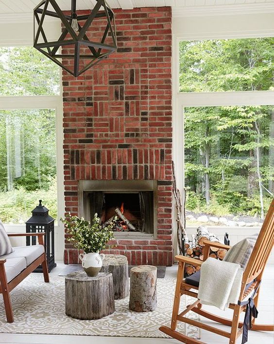a welcoming screened porch with a brick fireplace, simple stained wood furniture, neutral textiles and a faceted pendant lamp